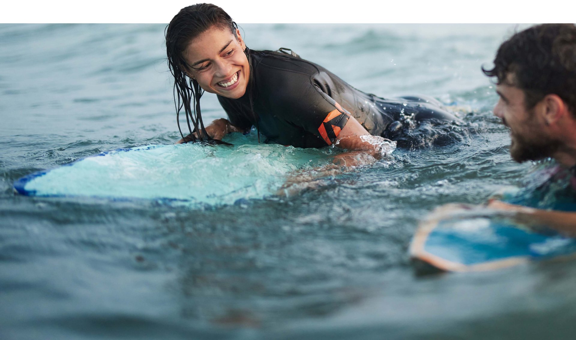 Woman on a surfboard smiling at her friend who is surfing too